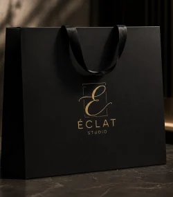 Branding salones de belleza — bolsa de packaging negra mate con logo Éclat Studio estampado en dorado y asas de cinta de seda